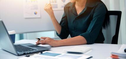 Asian Businesswoman Using laptop computer and working at office with calculator document on desk, doing planning analyzing the financial report, business plan investment, finance analysis concept. photo
