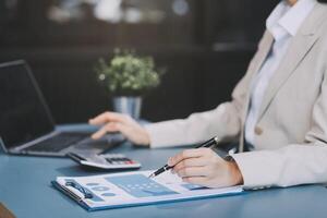 Asian Businesswoman Using laptop computer and working at office with calculator document on desk, doing planning analyzing the financial report, business plan investment, finance analysis concept. photo
