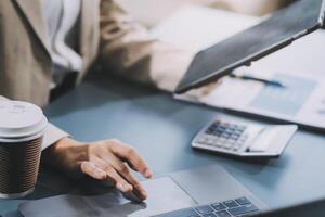 Asian Businesswoman Using laptop computer and working at office with calculator document on desk, doing planning analyzing the financial report, business plan investment, finance analysis concept. photo