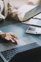 Asian Businesswoman Using laptop computer and working at office with calculator document on desk, doing planning analyzing the financial report, business plan investment, finance analysis concept. photo