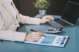 Asian Businesswoman Using laptop computer and working at office with calculator document on desk, doing planning analyzing the financial report, business plan investment, finance analysis concept. photo