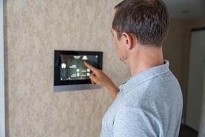 Man using tablet panel application for control smart home living. Wireless device controller for home automation IoT on the wall. High quality photo