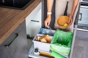 Woman throwing trash into household bins for waste sorting in the kitchen for recycle. Plastic, paper, bio and mixed waste. Sorting waste at home concept. High quality photo