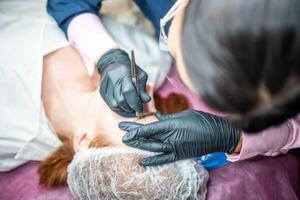 Procedure of eyebrow microblading. A master in black gloves is doing a blending needle of model's brow. High quality photo