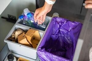 Hand of woman throwing trash into household bins for waste sorting in the kitchen for recycle. Plastic, paper, bio and mixed waste. Sorting waste at home concept. High quality photo