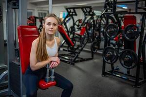 Young woman posing with dumbbells in her hands and works out in the gym performing an exercise photo