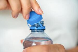 Bottle with stationary plastic cap in woman hand. The new design means the cap remains attached to the bottle after opening, making the entire package easier to collect and recycle. High quality photo