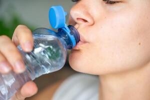 Young woman drinking from a bottle with stationary plastic cap. The new design means the cap remains attached to the bottle after opening, making the entire package easier to collect and recycle. photo