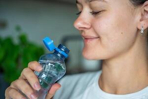 Young woman drinking from a bottle with stationary plastic cap. The new design means the cap remains attached to the bottle after opening, making the entire package easier to collect and recycle. photo