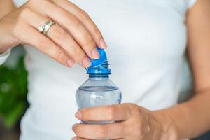 Bottle with stationary plastic cap in woman hand. The new design means the cap remains attached to the bottle after opening, making the entire package easier to collect and recycle. High quality photo