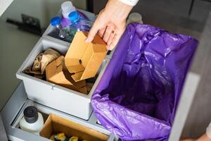 Hand of woman throwing trash into household bins for waste sorting in the kitchen for recycle. Plastic, paper, bio and mixed waste. Sorting waste at home concept. High quality photo