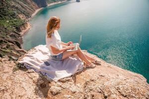 Freelance woman working on a laptop by the sea, typing away on the keyboard while enjoying the beautiful view, highlighting the idea of remote work. photo