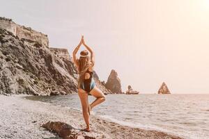 yoga en el playa. un contento mujer meditando en un yoga actitud en el playa, rodeado por el Oceano y rock montañas, promoviendo un sano estilo de vida al aire libre en naturaleza, y inspirador aptitud concepto. foto