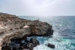 A rocky cliff overlooks the ocean, with the water crashing against the rocks. The scene is serene and peaceful, with the sound of the waves providing a calming atmosphere. photo