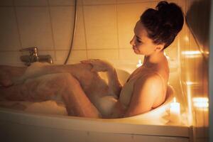 A woman is sitting in a bathtub with candles lit around her. Scene is relaxing and calming. photo