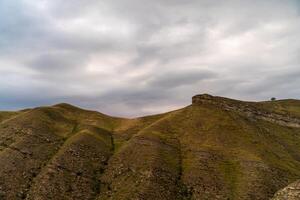 A mountain range with a cloudy sky in the background. The clouds are low and grey, giving the scene a somber and moody atmosphere. photo