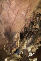 A man is walking through a cave with a large rock ceiling. The cave is dark and the man is holding a flashlight. photo