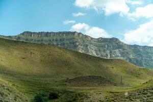 A mountain range with a green hillside. The sky is clear and blue. The mountain range is covered in grass and rocks. photo