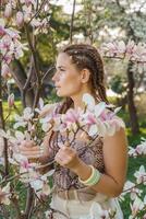 Magnolia flowers. Happy woman enjoys by blooming magnolia tree and sniffs it flowers with closed eyes in spring garden. Portrait. photo