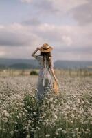 A woman is walking through a field of flowers, wearing a straw hat and carrying a basket. The scene is peaceful and serene, with the woman standing in the middle of the field photo