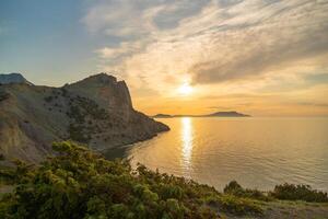A beautiful sunset over the ocean with a rocky cliff in the background. The sky is filled with clouds, creating a serene and peaceful atmosphere. photo