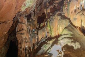 A cave with many stalactites and stalagmites. The cave is dark and the light is coming from the. photo