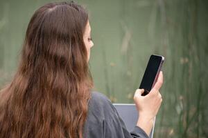 A woman is sitting on a dock with a laptop and a cell phone. She is talking on the cell phone while using the laptop. photo