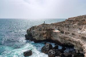 A rocky cliff overlooks the ocean, with the water crashing against the rocks. The scene is serene and peaceful, with the sound of the waves providing a calming atmosphere. photo