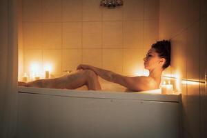 A woman is sitting in a bathtub with candles lit around her. Scene is relaxing and calming. photo