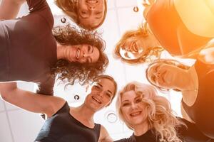 Low angle shot of smiling women looking at the camera, hugging, standing in a circle and doing team building photo
