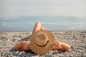 A woman is laying on the beach wearing a straw hat. She is relaxed and enjoying the sun. photo