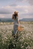 A woman is walking through a field of flowers, wearing a straw hat and carrying a basket. The scene is peaceful and serene, with the woman standing out against the backdrop of the colorful flowers. photo