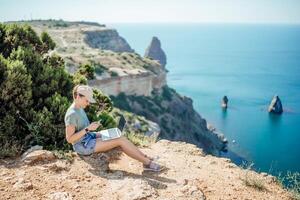 A woman is sitting on a rocky hillside overlooking the ocean photo