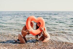 Two women are posing in the ocean with a heart-shaped inflatable raft photo