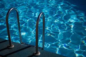 A metal ladder is in the water. The water is clear and calm. The ladder is in the middle of the pool. photo