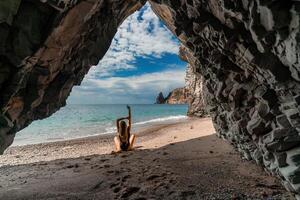 View of a woman in a black swimsuit from a sea cave Attractive woman enjoying the sea air sits on the beach and looks at the sea. photo