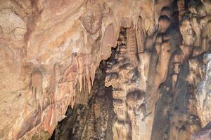 A cave with a lot of rock formations and stalactites hanging from the ceiling. Scene is mysterious and awe inspiring. photo
