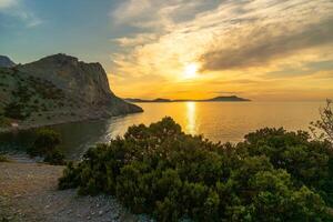 A beautiful sunset over the ocean with a rocky shoreline. The sky is filled with clouds and the sun is setting. photo