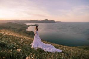 A woman in a white dress stands on a hill overlooking the ocean photo