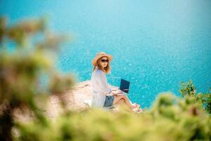 Freelance woman working on a laptop by the sea, typing away on the keyboard while enjoying the beautiful view, highlighting the idea of remote work. photo