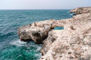 A rocky cliff overlooks the ocean. The water is calm and the sky is clear. The scene is peaceful and serene. photo