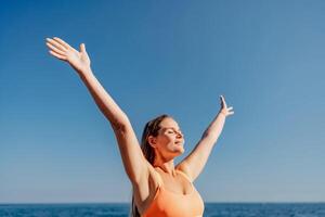 A woman is standing on the beach with her arms raised in the air, smiling photo