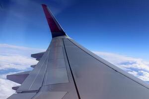 The wing of a jet plane and the scenery on the ground are visible through the porthole. photo