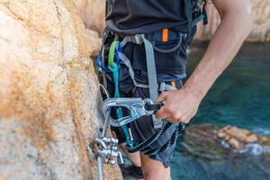 Climbing grips details young man's hand on rocks over the sea with rope and helmet. photo