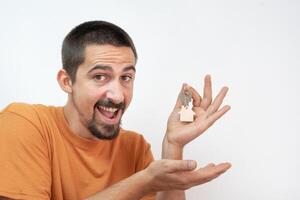 Happy young man smiling with the new home keys. Keychain in the shape of a wooden house. photo
