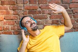Portrait of young handsome man listening to music with headphones against brick wall photo