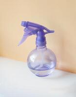 Purple ball spray bottle with water on white and peach beige background photo