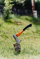 Axe with orange handle sticks out in hemp against the background of green grass photo