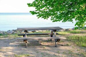 A wooden picnic table sits on the beach next to the water. photo