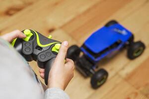 The boy is controling the blue toy car with a remote control. photo